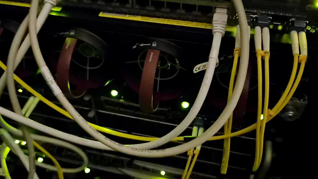 Ett bladserverkabinett med en nätverksswitch ovanför, patchkablar och tända portar i racket